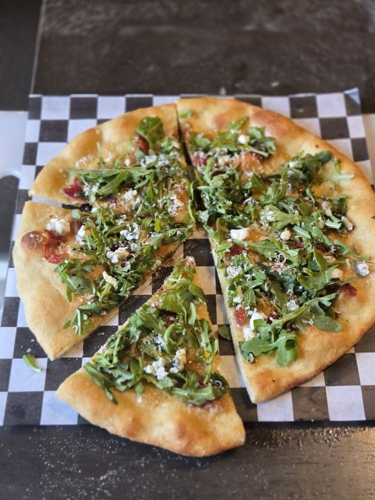 A slice pulled forward from a pizza topped with arugula and cured meat
