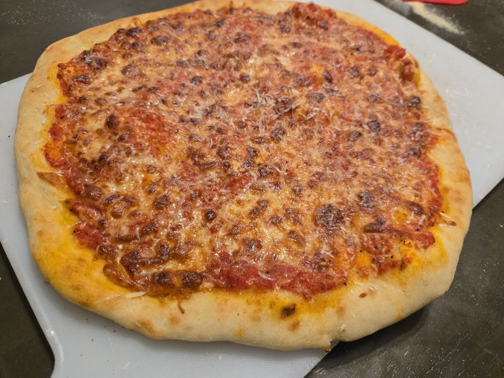 A classic cheese pizza with bubbly browned mozzarella on a flour-dusted cutting board